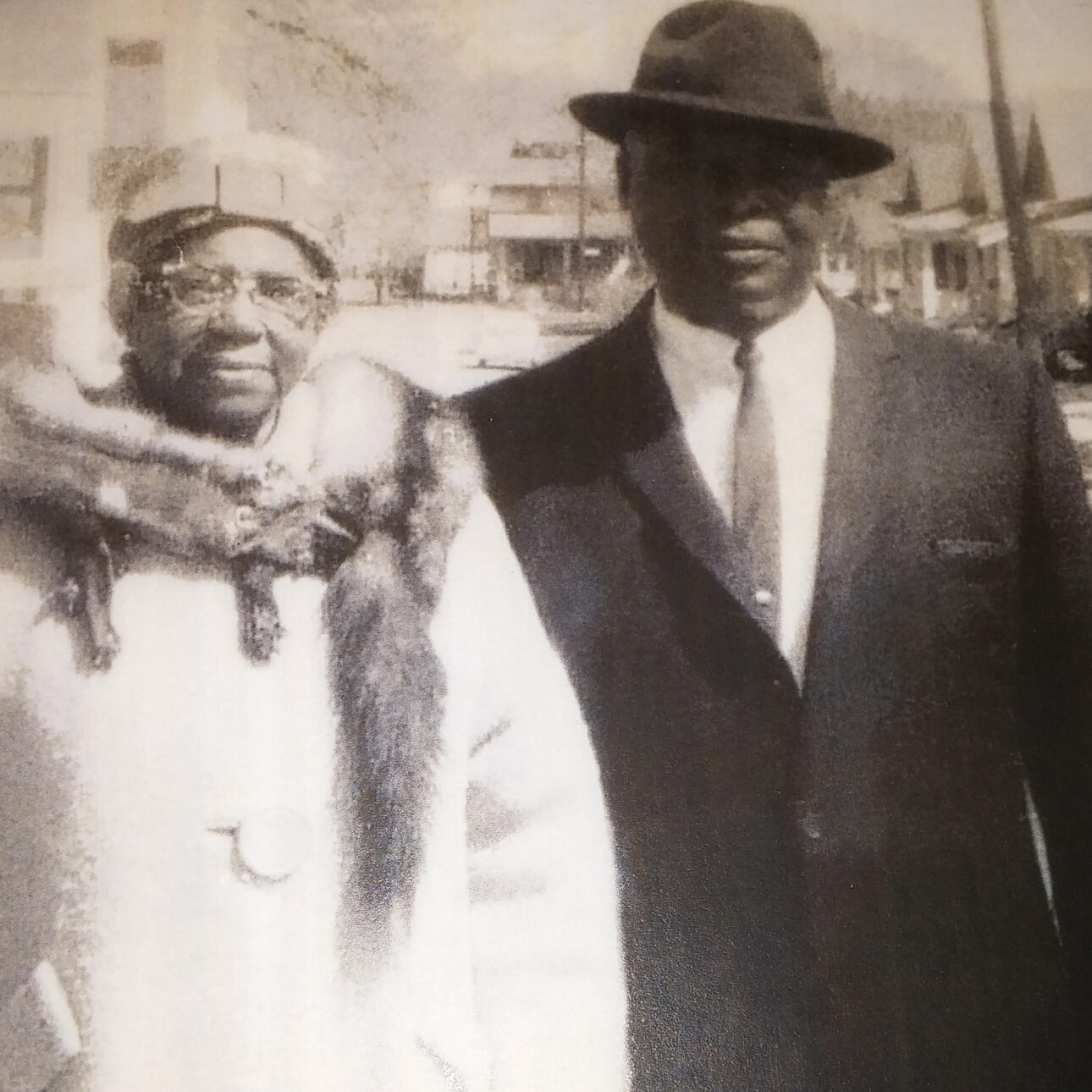 vintage photograph of older couple; the man is wearing a suit and hat and the woman is wearing a hat, coat and fox fur collar